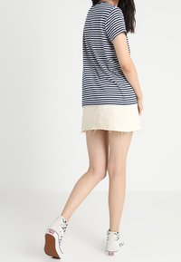 Námořnické a bílé pruhované tričko s krátkým rukávem, spárované s světle béžovou, roztrhanou džínovou sukní a teniskami na vysoké podrážce s kostkovaným vzorem.