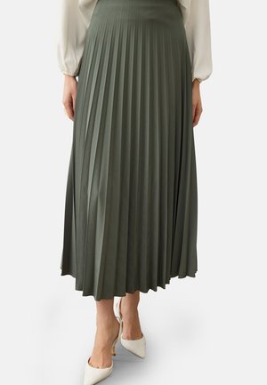 Donna che indossa una gonna midi plissettata a vita alta verde oliva abbinata a décolleté bianche con punta affilata e camicetta bianca a maniche lunghe.