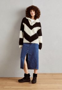 Pull en tricot surdimensionné à motif chevron noir et blanc, accompagné d'une longue jupe en denim avec une fente frontale et des bottines à plateforme noires.