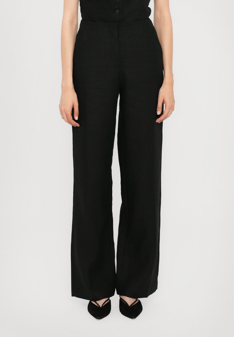 Black wide-leg trousers made of lightweight fabric, featuring a high waist and clean lines, paired with pointed black shoes.