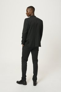Giacca e pantaloni neri, con una vestibilità sartoriale, tessuto liscio e un leggero lucido. Indossati con scarpe nere lucide.