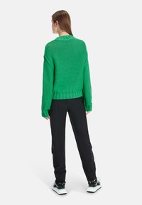 Grüner, voluminöser Strickpullover mit geripptem Halsausschnitt und Bündchen, kombiniert mit schwarzen, tapered Hosen mit elastischen Bündchen und seitlichen Taschen.