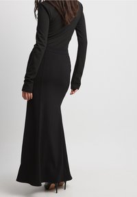 Schwarzes Langarmoberteil kombiniert mit einem knöchellangen schwarzen Rock. Glattes Material, taillierte Passform und subtile Glockenform am Saum. Tragen mit schwarzen Heels.