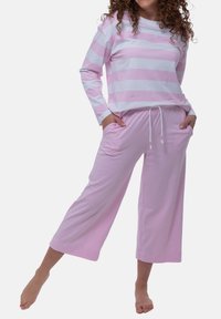 Completo pigiama rosa chiaro con una maglietta a maniche lunghe a righe orizzontali bianche e pantaloni rosa con cordino e tasche laterali. Materiale in morbido cotone.