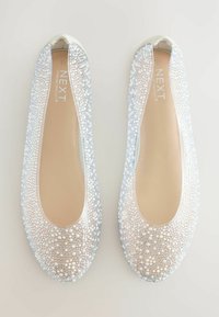 Ballerines avec un dessus transparent orné de grappes de perles blanches et argentées, bout rond et semelle intérieure beige clair.