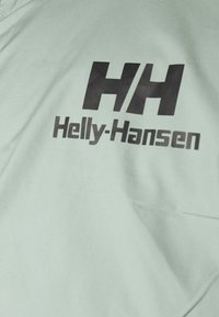 Tissu vert menthe arborant le logo noir "HH" et "Helly-Hansen" dans une typographie épurée. Texture lisse, design décontracté.