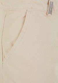 Beige denim stoff som viser en nærbilde av en lomme og søm detaljer, med en glatt tekstur og subtile ribber.