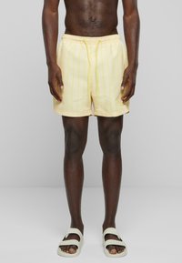 Shorts de bain rayés jaunes avec une taille élastique et un cordon de serrage. Le tissu a une texture lisse, idéal pour les activités aquatiques.
