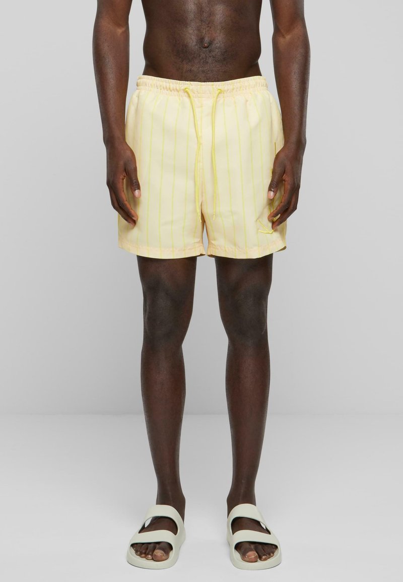 Shorts de bain rayés jaunes avec une taille élastique et un cordon de serrage. Le tissu a une texture lisse, idéal pour les activités aquatiques.