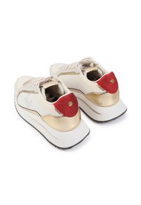 Zapatillas con parte superior de cuero blanco, acentos dorados, lengüetas traseras texturizadas en rojo y diseño de cordones. Suela gruesa blanca y negra.