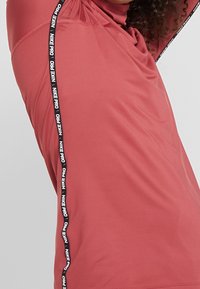 Red athletic shirt with black "NIKE PRO" tape down the side. Smooth, stretchy fabric with a fitted design, featuring a slightly wrinkled texture.