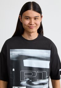 Sort t-shirt med et stort grafisk tryk, der viser et sløret racingbillede, hvide textelementer og en afslappet pasform.