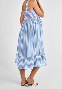 Un vestido de verano a rayas azul y blanco con un cuerpo fruncido, tirantes ajustables y un dobladillo de volantes en capas, combinado con sandalias ligeras.