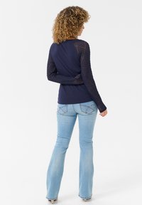 Navy long-sleeve top with textured mesh sleeves paired with light blue flared jeans, featuring subtle stitching on the pockets.
