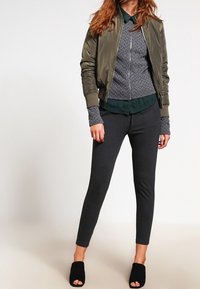 Olivově zelená bomber bunda přes texturovaný šedý svetr, doplněná tmavě šedými legínami a černými pantoflemi s otevřenou špičkou. Slim fit, ležérní styl.