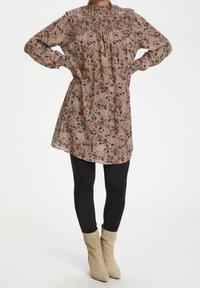 Robe à manches longues fleurie en rose doux, avec un col montant smocké et une coupe décontractée, accompagnée de leggings noirs et de bottines beiges.
