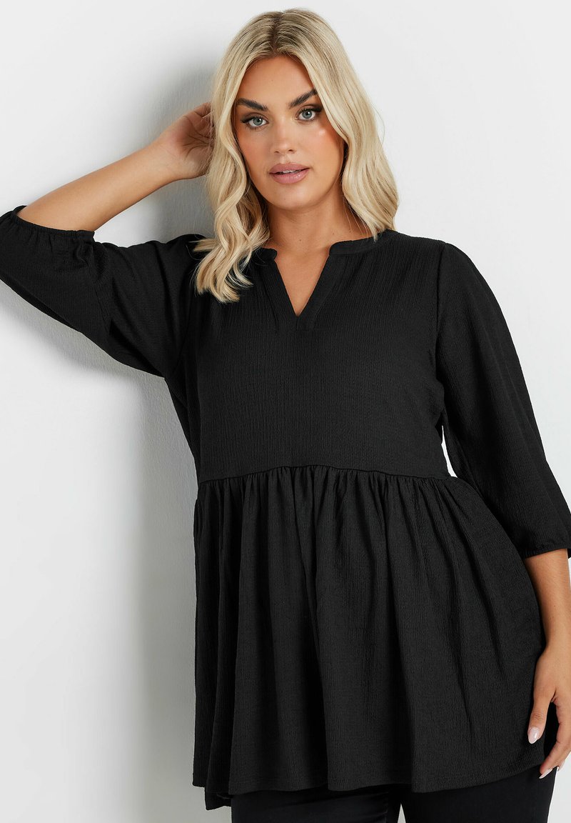 Tunic nera con tessuto strutturato, dotata di un orlo plissettato e scollo a V. Ha maniche a trequarti e una vestibilità comoda.