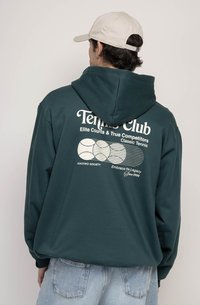 Zelená mikina s kapucňou a grafickým motívom na zadnej strane, ktorý obsahuje text "Tennis Club" a ilustrácie tenisových loptičiek. Kapucňa a voľný strih, kombinovaná s svetlým džínsovým materiálom.