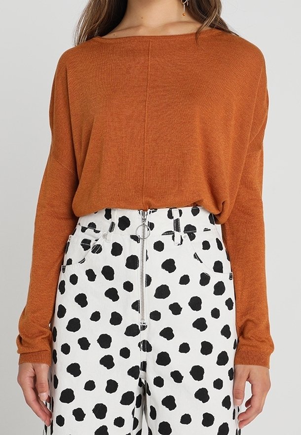 Rostfärgad stickad tröja med lös passform och båtutskärning, i kombination med vita byxor med stora svarta prickar och dragkedja framtill.