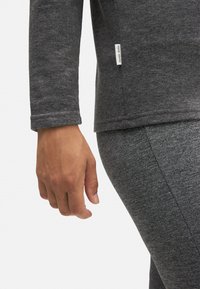 Top de manga larga gris oscuro con un acabado suave y texturizado y una pequeña etiqueta en el dobladillo, combinado con leggins ajustados gris oscuro a juego.