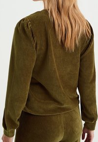 Top in velluto a coste verde oliva con texture a coste verticale, maniche lunghe e spalle arricciate. Il retro presenta una silhouette liscia e aderente.