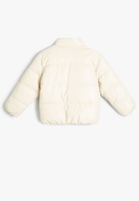 Cremefarvet puffjakke med en blank finish, der har en stående krave, lange ærmer og vandret syninger for tekstur.