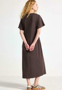Brun midi kjole med korte ærmer, der har en lige skæring og søm i midten bagpå. Fungerer godt sammen med beige og brune sneakers.
