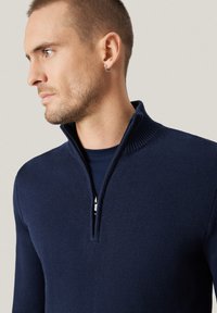 Granatowy dzianinowy sweter z suwakiem do połowy, z prążkowanym kołnierzem i mankietami. Charakteryzuje się gładką fakturą oraz srebrnym suwakiem przy szyi.