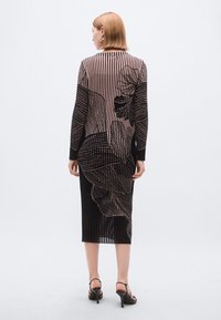 Robe en maille noire et rose avec des rayures verticales et de grands motifs floraux. Manches longues, coupe mi-longue et texture côtelée.