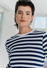 Tricou cu dungi navy și alb, cu guler rotund, realizat dintr-un material moale. Are mâneci scurte și o croială lejeră.
