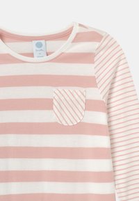 Lett langermet topp i myke krem- og rosa striper, med en stripete lomme og rund hals. Laget av økologisk stoff.