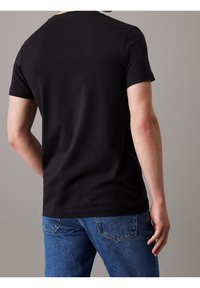 Svart bomullströja med korta ärmar och rundad halsringning. Bärs med blå denimjeans, vilket visar en avslappnad passform och minimalistisk design.