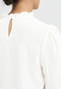 Witte blouse van een textuurstof, met een volanten kraag en een opening met sleutelgat aan de achterkant. De pofmouwen versterken het zachte, vrouwelijke ontwerp.