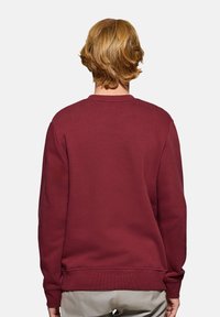 Burgundy sweatshirts i mjukt material med rund hals, insydda ärmar och ribbade muddar. Slät yta utan synliga mönster eller detaljer.