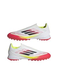 Weiße Fußballschuhe mit einem Slip-On-Design, das pinke Akzente, schwarze Streifen und ein strukturiertes Obermaterial aufweist. Multidirektionale Noppen auf der Sohle.
