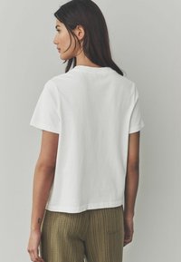 T-shirt en coton blanc à manches courtes, avec un col rond et une coupe décontractée, associé à un pantalon à rayures vertes et dorées.}}