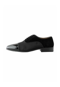Schwarze Herrenschuhe mit glänzendem Zehenteil, strukturiertem Mittelteil, Wildlederabsatz und Schnürdesign vor weißem Hintergrund.