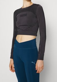 Svart cropped långärmad topp med "PUMA"-logotyp på bröstet och längs ärmarna, i kombination med blå högmidjade leggings som har en logotyp.
