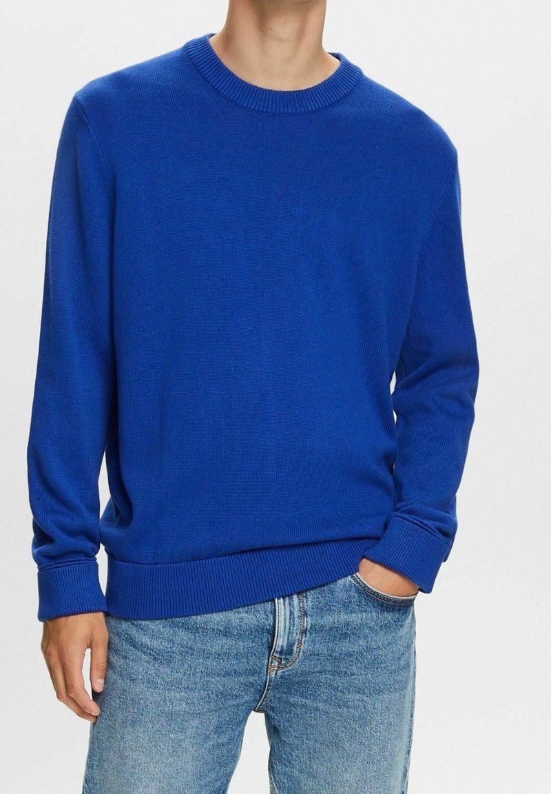 Pull bleu tricoté avec un col rond, des poignets et un ourlet côtelés, présentant une texture lisse et une coupe décontractée, associé à un jean bleu clair.