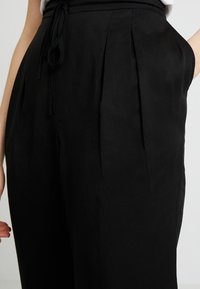 Černé kalhoty s volným střihem, s plisováním, elastickým pasem se šňůrkou a bočními kapsami, vyrobené z hladké látky.
