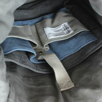 Borsa a righe con tessuto grigio scuro e blu. Presenta una tracolla grigia e un'etichetta con le istruzioni per la cura. Scomparti interni per l'organizzazione.