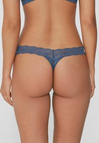 Blaue Spitzen-Tanga-Unterwäsche mit gewelltem Rand und Blumenmuster, ausgestattet mit einem schmalen Bund, entworfen für minimale Bedeckung.