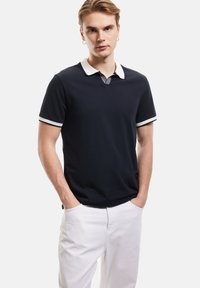 Laivaston värinen polo-paita, jossa on valkoinen kaulus ja raidoitukset, lyhyet hihat, puuvillamateriaalia, käytetään valkoisten housujen kanssa, rento malli.