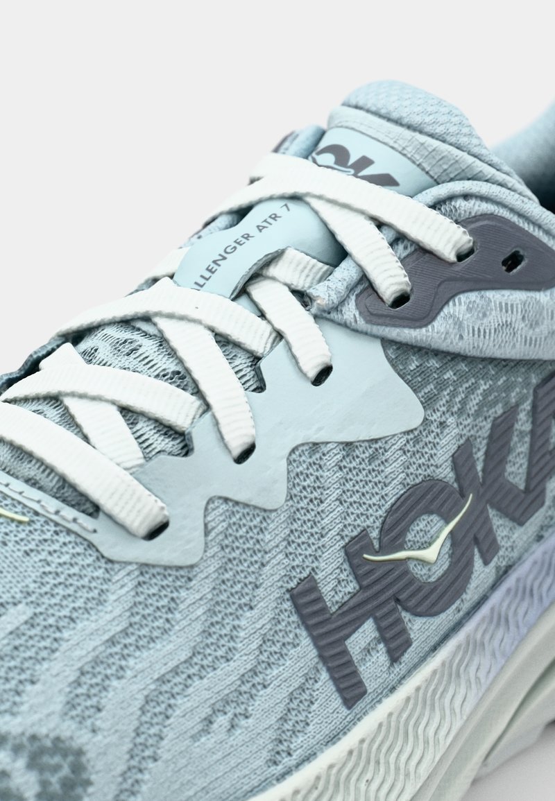 Las zapatillas HOKA Challenger ATR 7 de color azul claro presentan un upper texturizado, cordones blancos y un diseño de acento en forma de ola en gris.