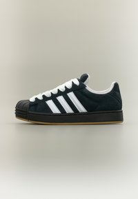 Black suede sneaker with white laces and three white stripes. Features a rubber toe cap and a gum rubber sole. Low-top design.
