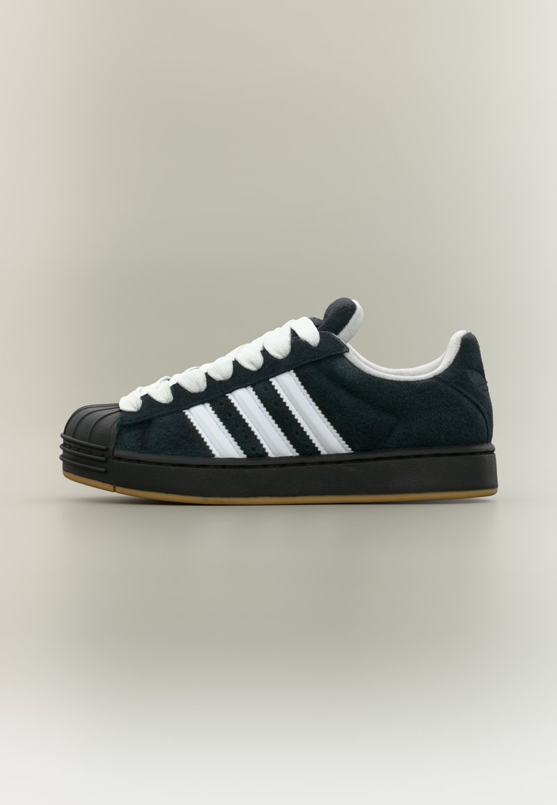 Black suede sneaker with white laces and three white stripes. Features a rubber toe cap and a gum rubber sole. Low-top design.