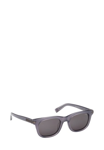 Harmaansävyiset aurinkolasit puoliläpinäkyvällä kehyksellä. Neliönmuotoiset linssit ja metallikoristeet sankoissa. Sileä pinta, minimalistinen muotoilu.