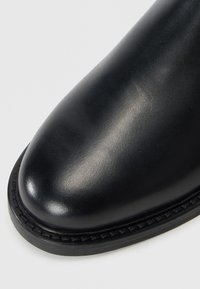 Black leather boot with a rounded toe, smooth texture, and contrasting stitched leather sole. Standard height with no visible hardware.