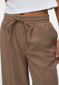 Joggers marrones con canalé, cintura elástica y cierre de cordón. Presenta costuras verticales para un look más ajustado y una textura suave.