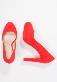 Röda mocka högklackade pumps med rund tå, vinklad skärning på sidan och tjock klack. Slätt foder invändigt och en minimalistisk logotypdetalj.